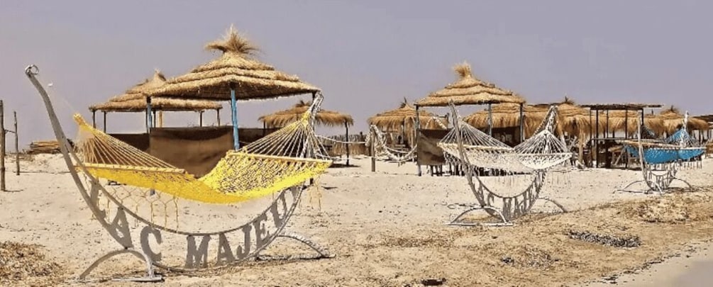 A desert landscape with hammocks and thatched-roof structures. 1