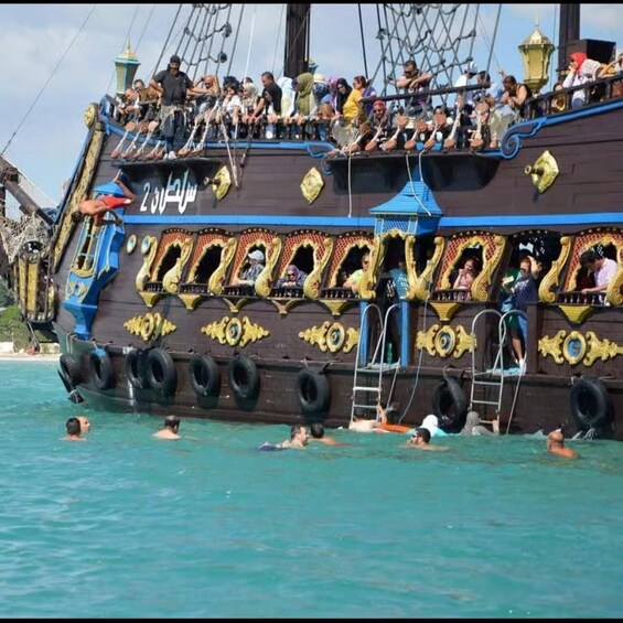 A large, ornately decorated ship with people on deck and swimmers in the water. 5