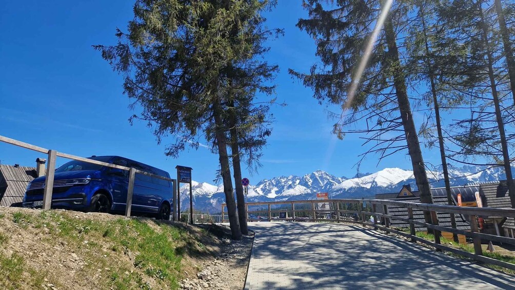 A blue bus parked on a gravel path with a mountain backdrop. 2