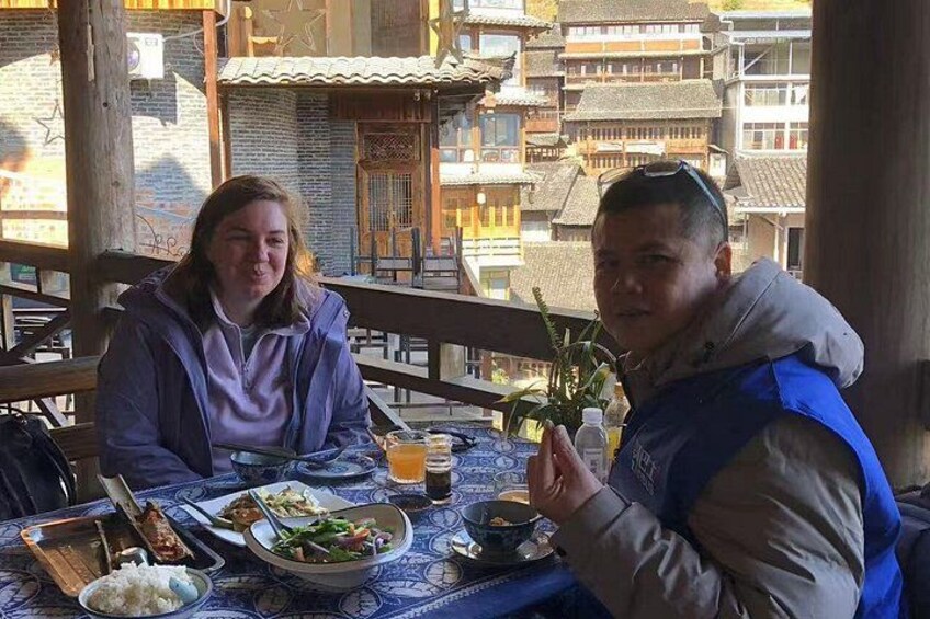 Two people dining at an outdoor table with traditional architecture in the background. 4