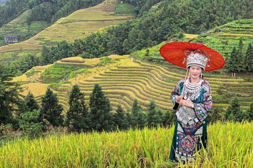 A person in traditional attire standing in a rice field with terraced hills in the background. 1