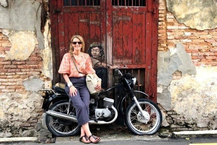 A person sitting on a motorcycle in front of a weathered building with a red door. 4