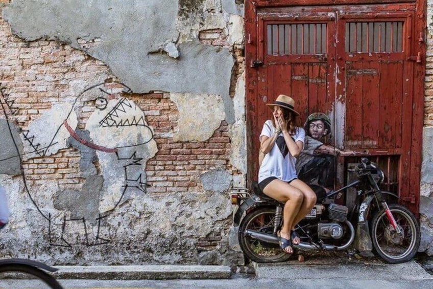 A motorcycle parked in front of a red door, a mural on the wall, and a person sitting on the motorcycle. 1