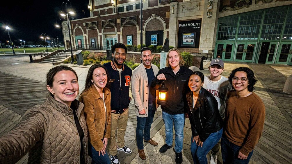 A group of people taking a selfie in front of a theater with a brick facade and green windows. 3