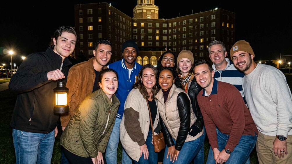 A group of people posing in front of a large building with illuminated windows at night. 1