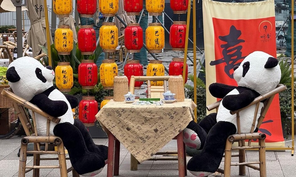Two panda plush toys seated at a table with traditional Chinese decorations and lanterns in the background. 4