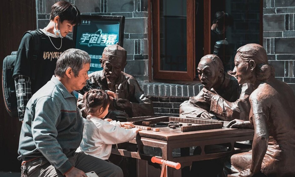 A group of people playing a board game at a table with a brick wall and a poster in the background. 1