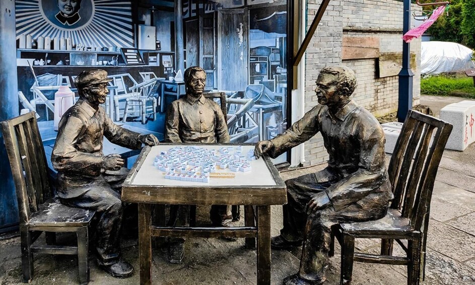 Three bronze statues of men seated at a table with a board game. 3