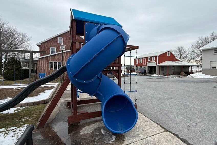 A blue slide at a playground with a brick building in the background. 2