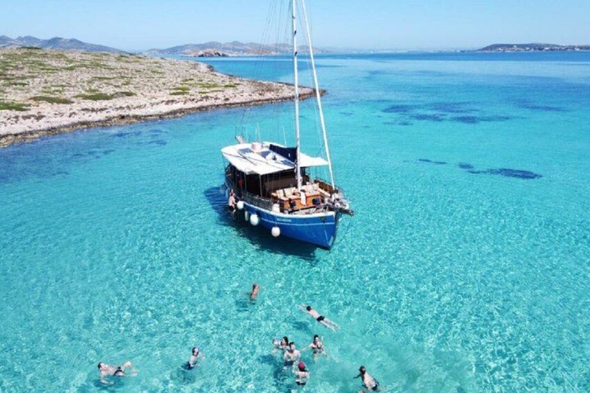 A sailboat on clear turquoise water with people swimming around it. 5