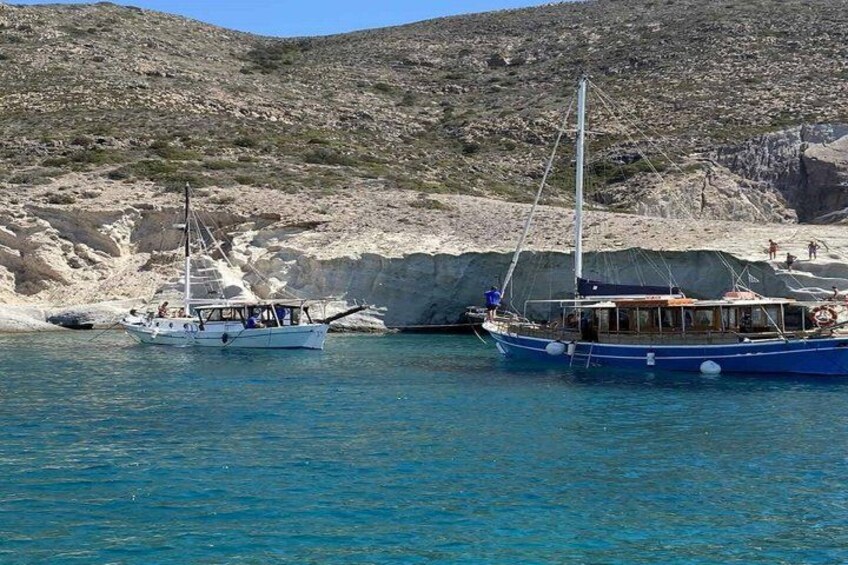 Two boats docked near a rocky coastline with clear blue water. 4