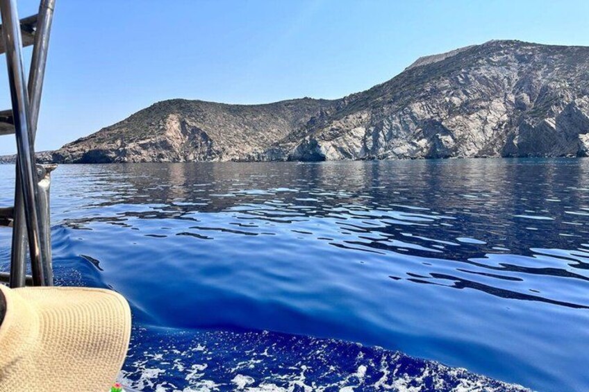 A boat on calm water with a rocky coastline and a mountain in the background. 3