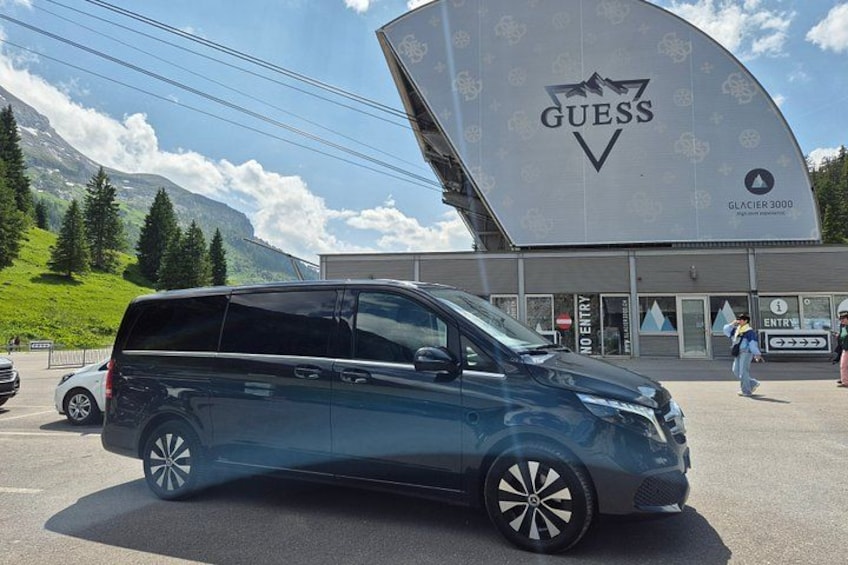 A blue SUV parked in front of a building with a 'GUESS' logo and a sign for 'Glacier 3000'. 3