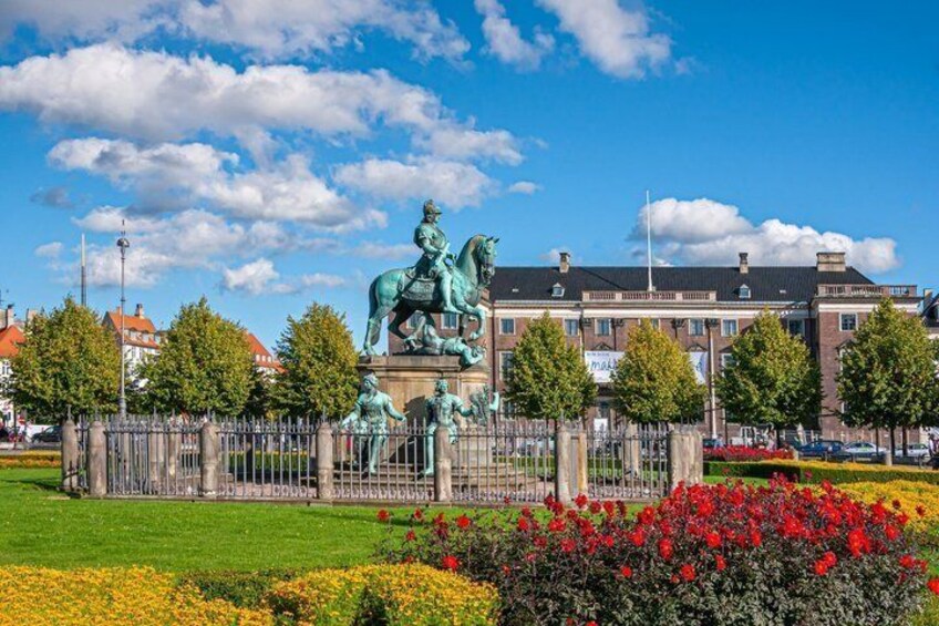 En staty föreställande en person på hästryggen, ett staket och en byggnad med ett rött tak i bakgrunden. 2