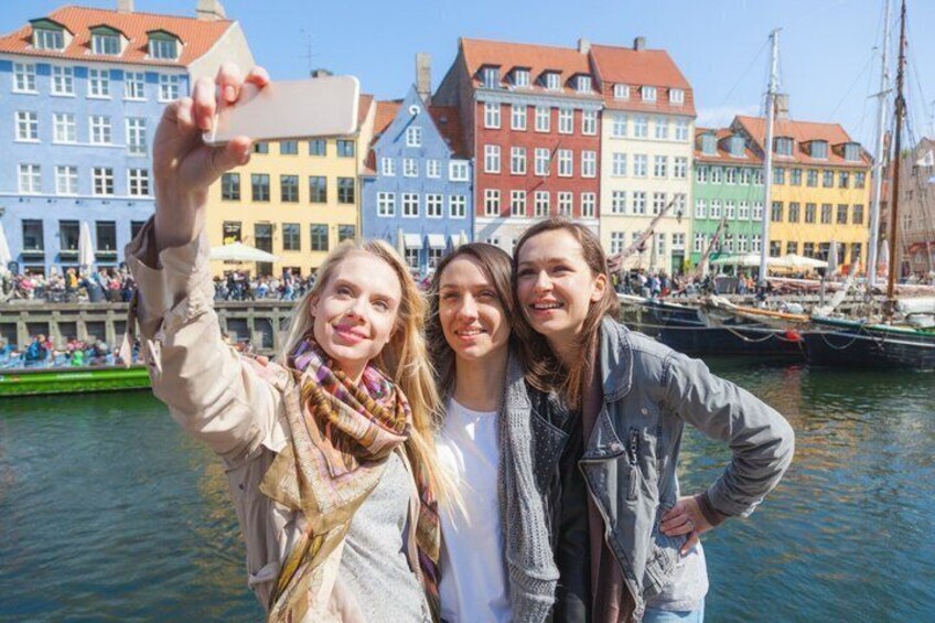 Tre personer som tar en selfie med färgglada byggnader och båtar i bakgrunden. 1