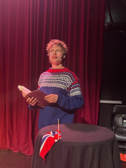 A person holding a book on a stage with a red curtain backdrop. 5
