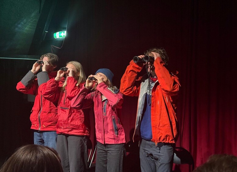 A group of people on stage with red jackets, some holding binoculars. 3