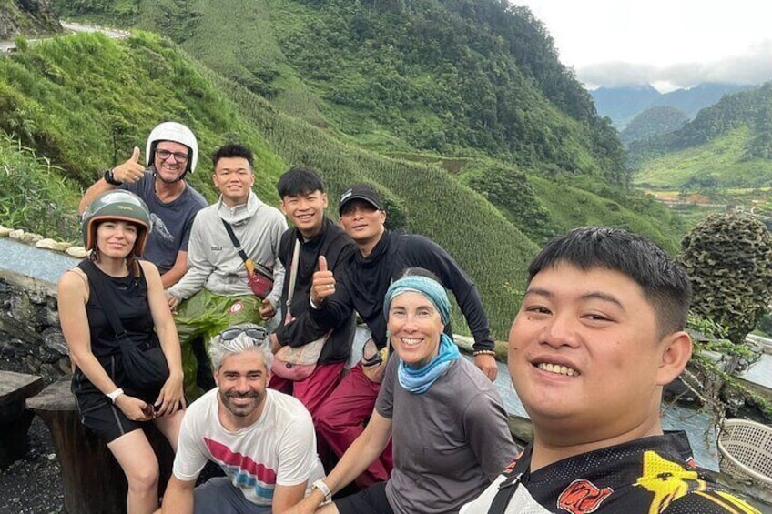 A group of people on a mountain trail with lush greenery and a valley in the background. 1