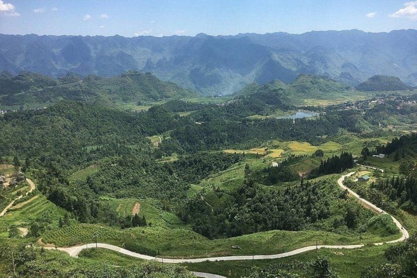 A mountainous landscape with winding roads, dense greenery, and distant water bodies. 2