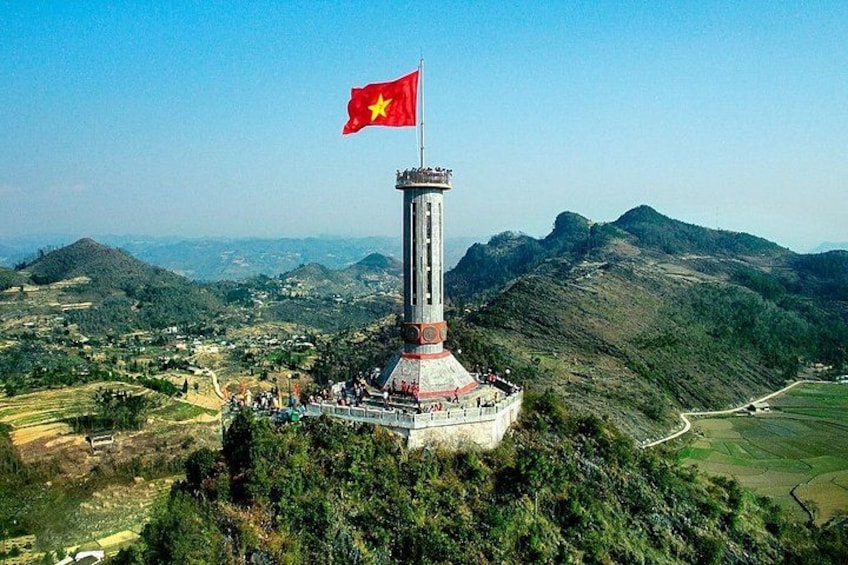 A tower with a flag, surrounded by green hills and a clear sky. 4