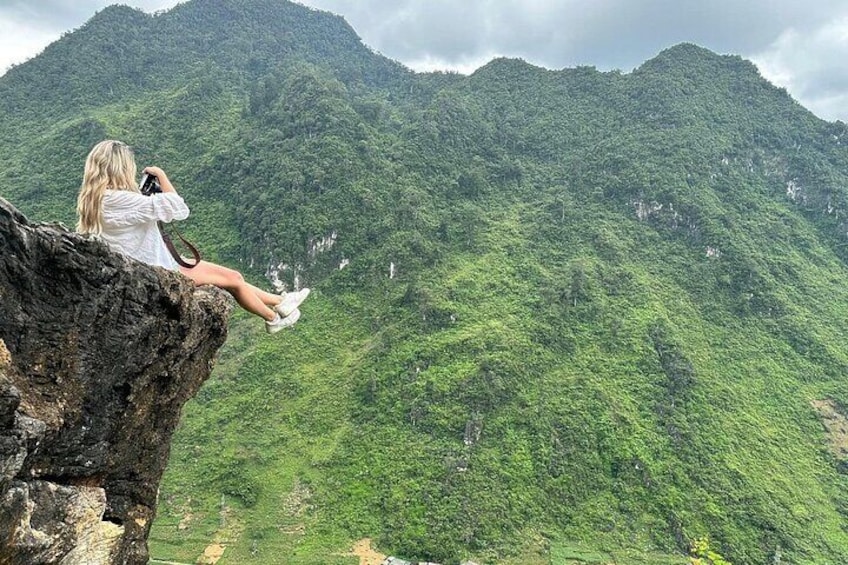 A person sitting on a rock with a mountain in the background. 4