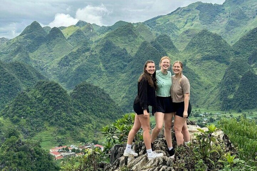 Three people standing on a rocky outcrop with a mountainous landscape in the background. 1