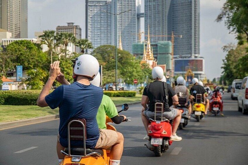 A group of motorcyclists riding on a city street with buildings and greenery in the background. 4