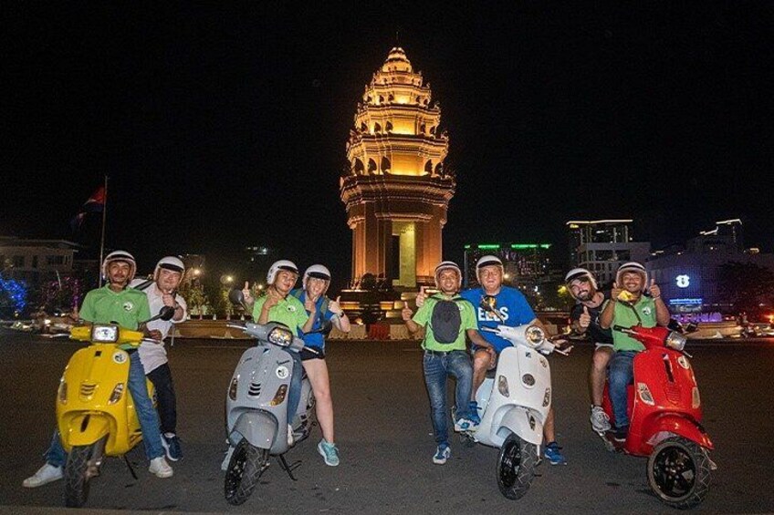 A group of people on scooters in front of a illuminated tower at night. 1