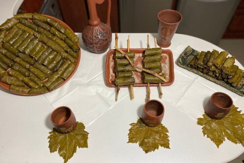 Un tavolo con diversi piatti di foglie di vite ripiene, una pentola di terracotta e piccole tazze. 4