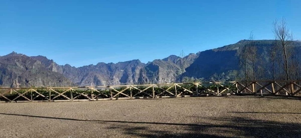 A wooden bridge over a gravel path with mountains in the background. 1