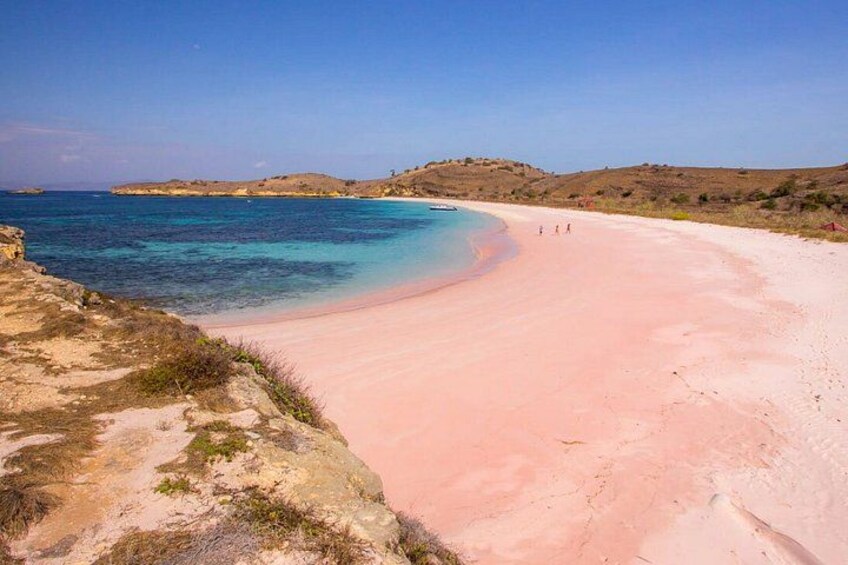 A beach with clear turquoise water, a pinkish sand, and distant hills. 4