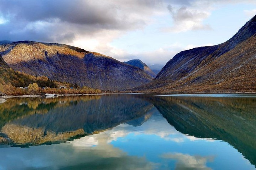 A calm lake reflecting mountains, clear sky, and a small building near the shore. 5