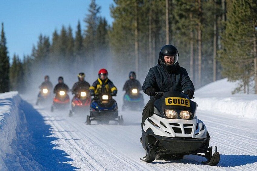 A snowmobile race with participants on a snowy track surrounded by trees. 4