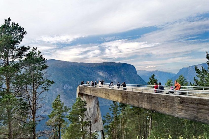 A wooden bridge with people walking on it, surrounded by mountains and trees. 3