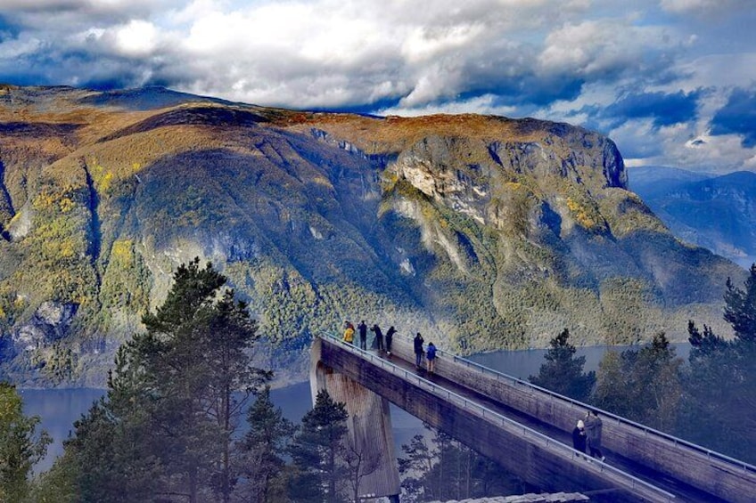 A bridge with people walking across it, overlooking a mountainous landscape with a lake below. 4