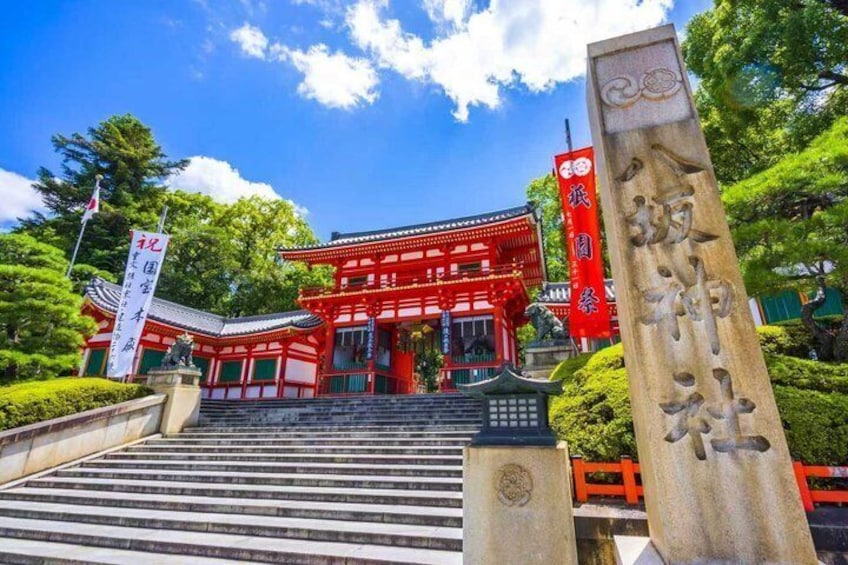 Ett traditionellt japanskt tempel med röda och vita byggnader, ett stenmonument med inskriptioner och en klarblå himmel. 3