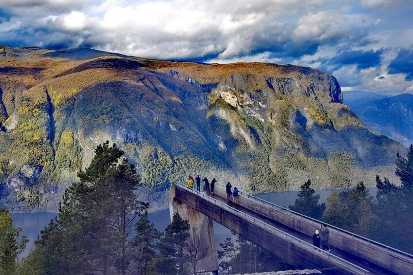 A bridge with people walking across it, overlooking a mountainous landscape with a lake below. 2