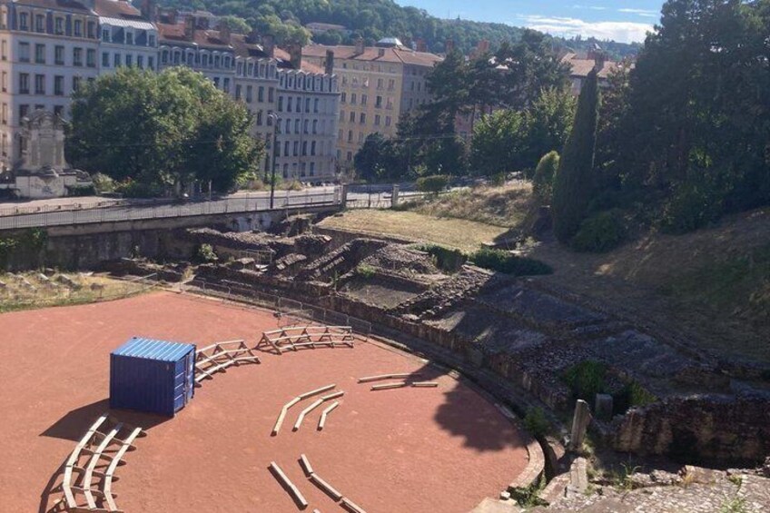 Ancient ruins with a circular amphitheater, a blue storage box, and a river in the background. 2