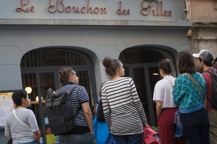 A group of people standing outside a building with the sign 'Le Bouchon des Filles.' 1