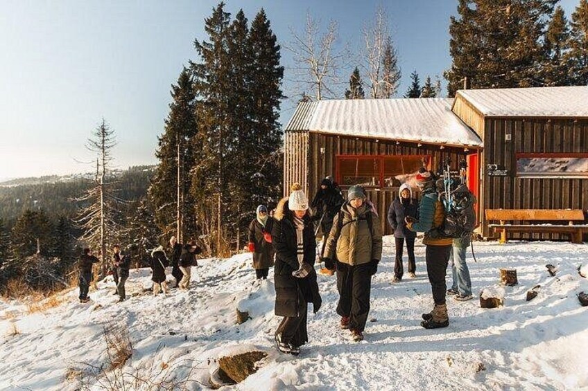 A group of people in winter clothing walking on a snowy path with a wooden cabin and trees in the background. 4
