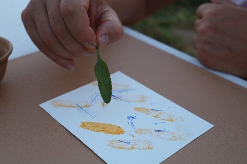 Eine Hand hält ein grünes Blatt über Papier mit gelben und blauen Kritzeleien. 3