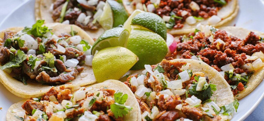 A plate of tacos with meat, onions, cilantro, and lime wedges. 5