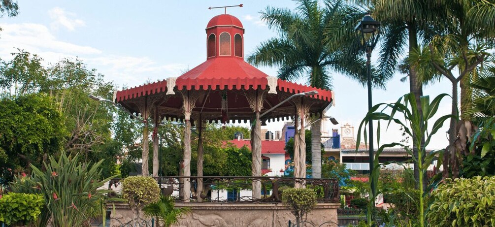 A red gazebo with a dome roof, surrounded by palm trees and greenery. 3