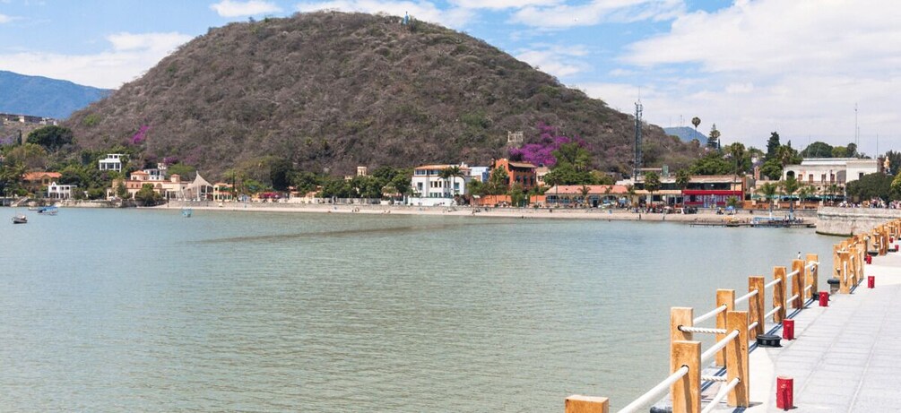 A calm lake with a wooden pier, buildings, and a hill in the background. 2