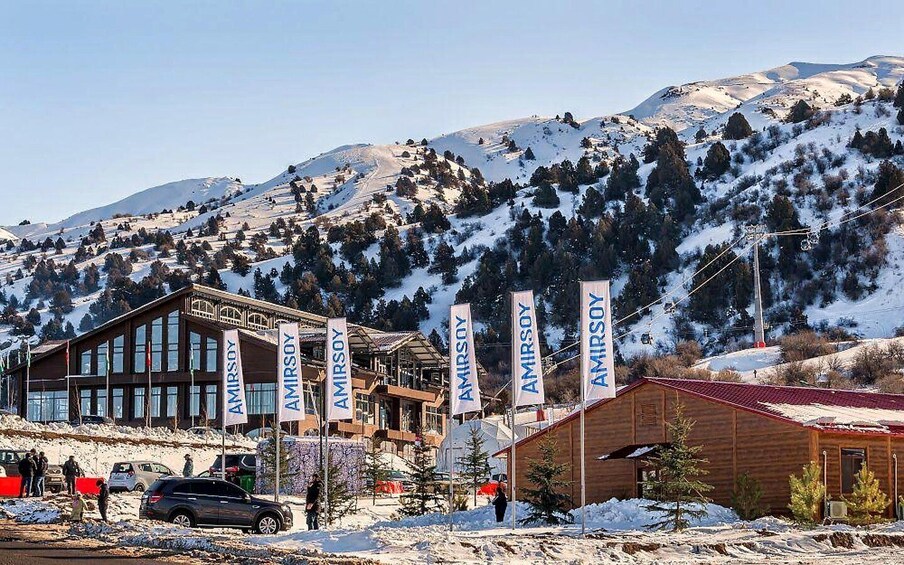 A snowy mountain resort with wooden cabins and a large building with multiple flags. 2