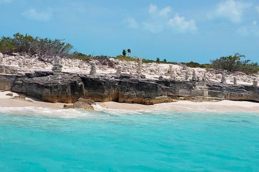 A beach with white sand and turquoise water, rocky cliffs, and sparse vegetation. 2