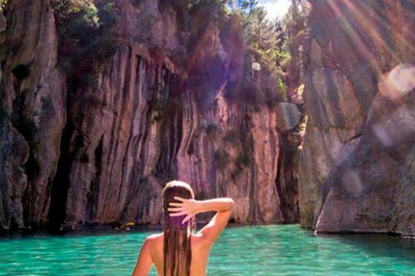 Una persona con traje de baño parada en aguas turquesas cristalinas, con acantilados rocosos al fondo. 1
