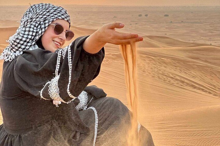 A person in traditional attire sitting on a sand dune, holding sand. 4