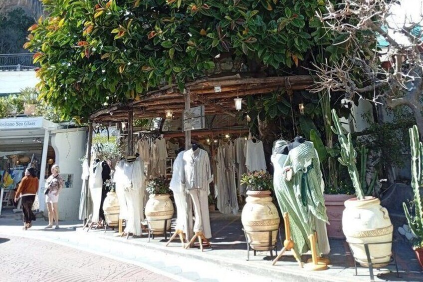 A street with mannequins dressed in vintage clothing, potted plants, and a building with a sign. 5