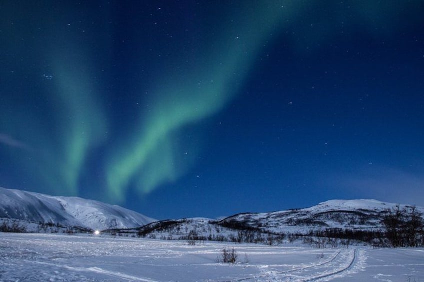 A snowy landscape with a clear night sky, a visible aurora, and a distant light source. 1